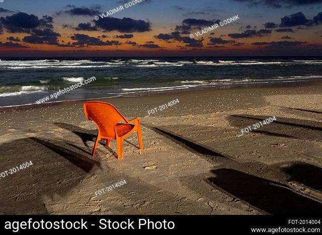 Orange lawn chair on sandy beach at dusk, Bat Yam, Israel