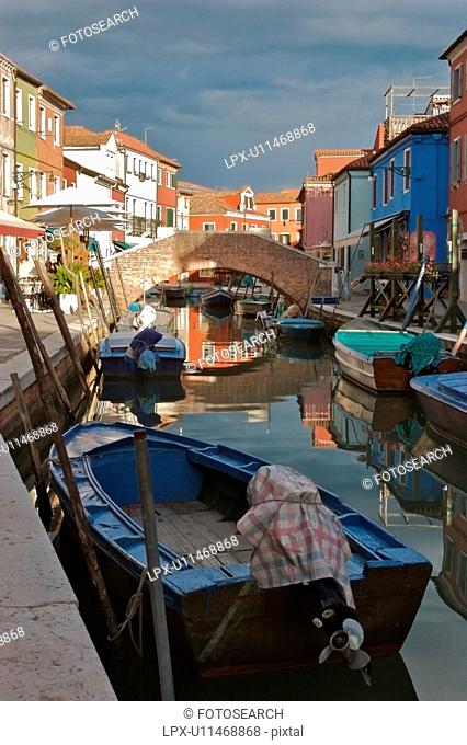 Boats moored along Burano canal , in sunlight before an evening summer storm