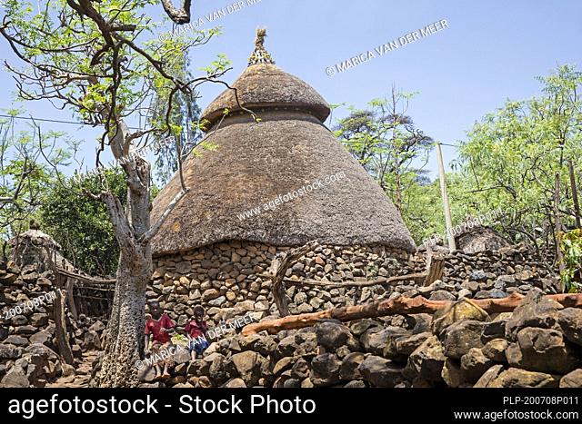 Two black children in front of traditional stone hut with thatched roof of the Konso / Xonsita tribe, south-western Ethiopia, Africa