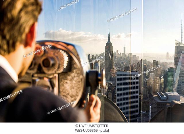 USA, New York City, man looking through coin-operated binoculars on Rockefeller Center observation deck