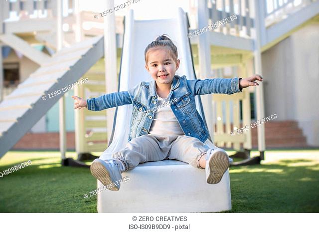 Girl at preschool, portrait sitting on playground slide in garden