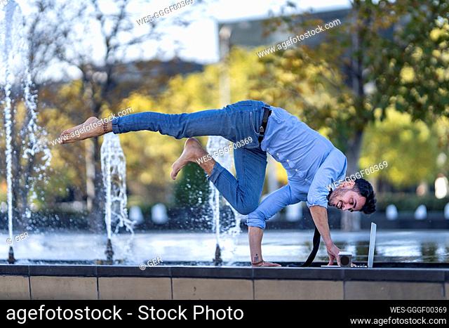 Young businessman using laptop while doing handstand on retaining wall