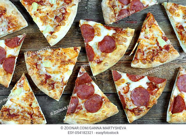 Pizza-background. Pepperoni pizza and Hawaiian pizza cut into pieces on a wooden table. Close-up, top view