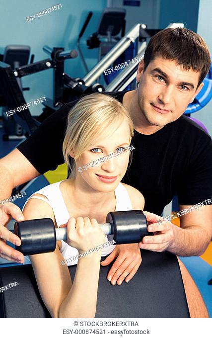 Photo of blonde woman holding dumbbell with man near by