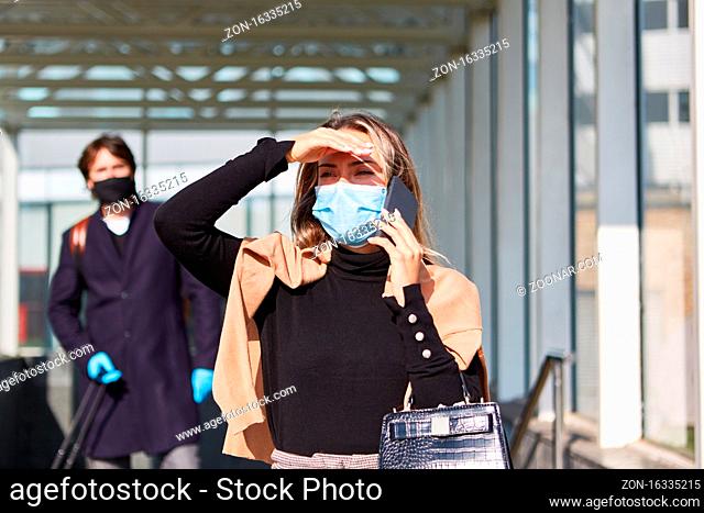 Business Frau auf Dienstreise mit Smartphone und Maske wegen Covid-19 Pandemie