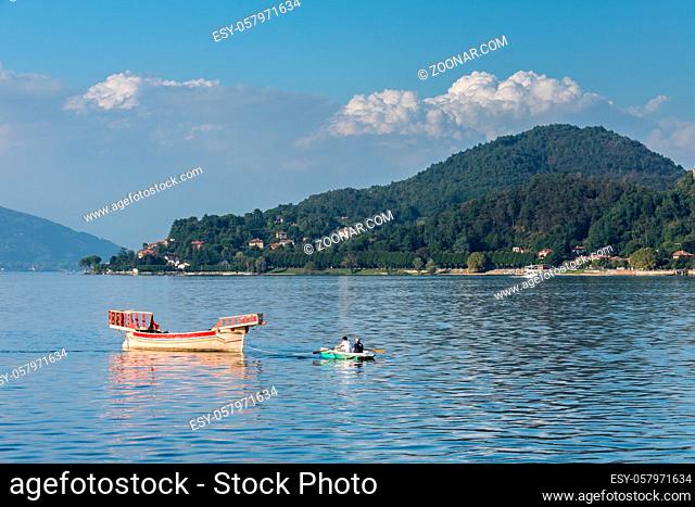 Rowing boat pulling a traditional boat on Lake Maggiore Piedmont Italy