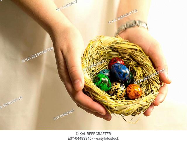 straw nest with eggs painted in different colors lie in the palm of the hand