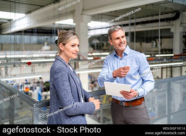 Businessman with digital tablet and businesswoman talking in factory