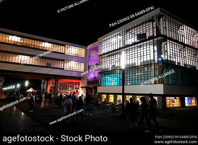 02 September 2023, Saxony-Anhalt, Dessau-Roßlau: Visitors walk by the colorfully illuminated Bauhaus. The two-day Bauhaus Festival will feature spatial and art...