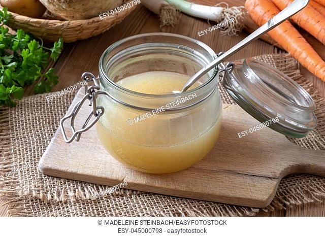 Chicken bone broth in a glass jar, with fresh vegetables in the background