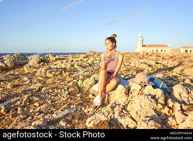 Young woman sitting on rocky beach, relaxing, Menorca, Spain
