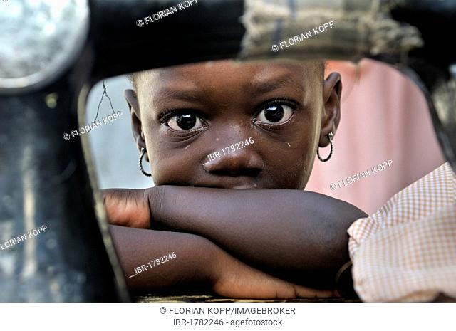 Little girl hiding behind an old mechanical sewing machine, camp for victims of the January 2010 earthquake, Croix-des-Bouquets district, Port-au-Prince, Haiti