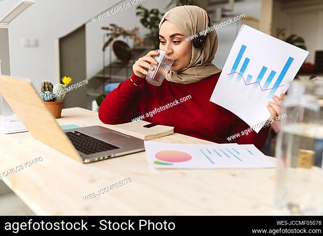 Businesswoman drinking water and working on laptop at home