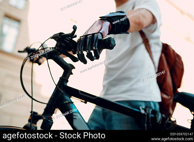 Young disabled man with artificial prosthetic hand in casual clothes riding bike