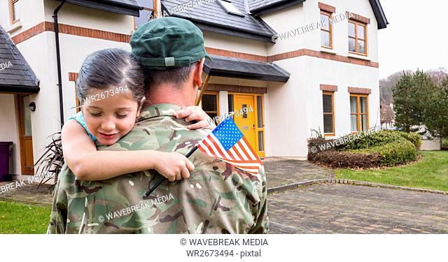 American soldier carrying girl in front of a house