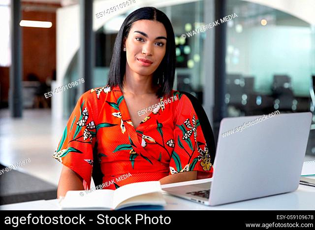 Portrait of smiling mixed race businesswoman sitting in front of laptop