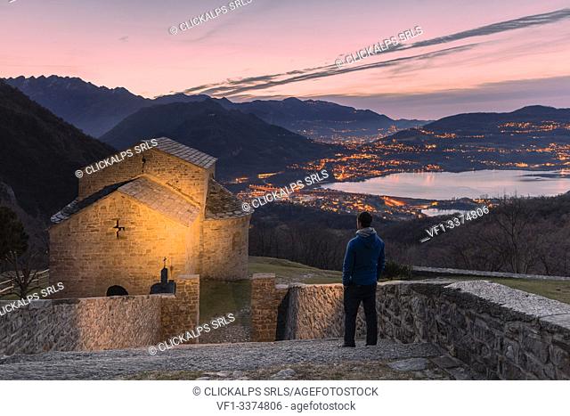 A tourist admiring the abbey of San Pietro al Monte, an ancient monastic complex of Romanesque style in the town of Civate at sunrise, Lecco province, Lombardy