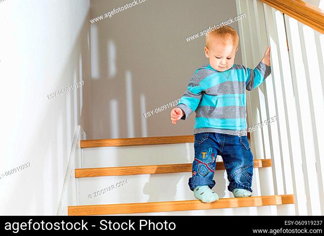 The toddler blond boy on the stairs. The boy carefully goes down the stairs at home