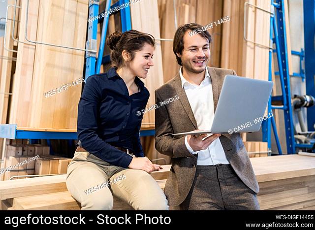 Smiling businessman using laptop while standing by colleague at industry