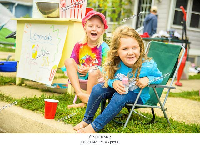 Candid portrait of two smiling girls selling lemonade and popcorn at yard sale