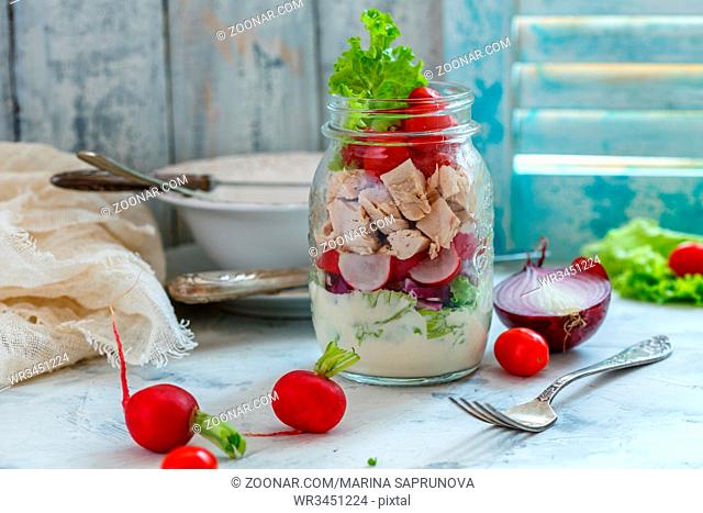 Homemade salad with chicken, vegetables and sauce in a glass jar on a white table, selective focus