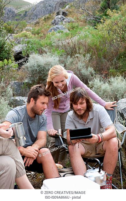 Group of young hikers taking a break, looking at hand held computer
