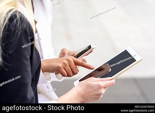 Businesswoman pointing at digital tablet while using mobile phone by colleague at city