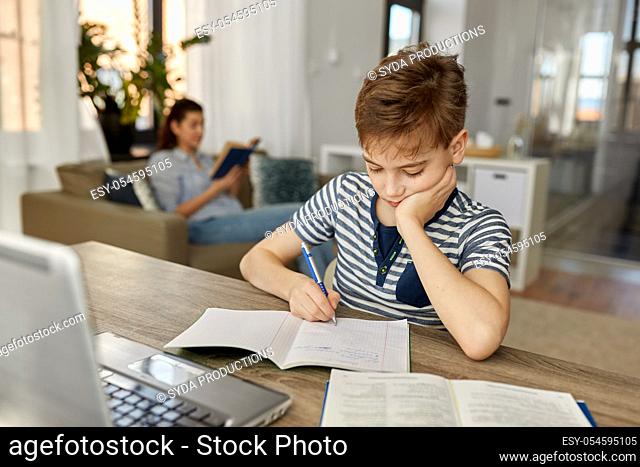 student boy with book writing to notebook at home