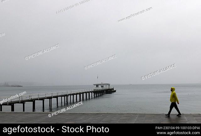 04 January 2023, Schleswig-Holstein, Kiel: A walker is on the Kiellinie at the Kiel Fjord in cloudy weather and light rain