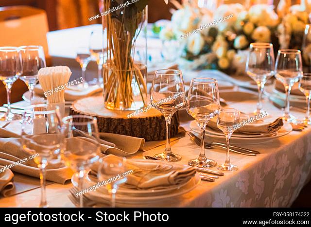 Exquisitely served table for wedding celebration. Piece of wooden trunk used as stand for glass vase, placed in the middle of table