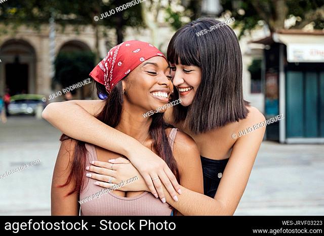 Smiling young woman embracing friend on footpath