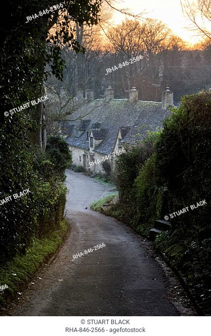View down lane to Arlington Row Cotswold stone cottages at dawn, Bibury, Cotswolds, Gloucestershire, England, United Kingdom