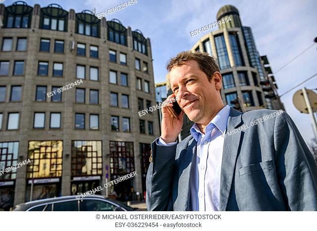 Close up look of a middle age businessman standing in front of the office building while talking on his phone