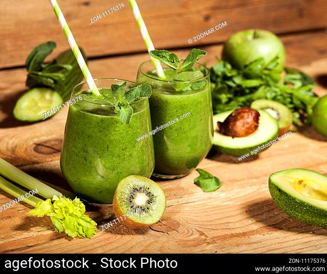 Freshly blended green smoothie in glasses with straws on wooden background