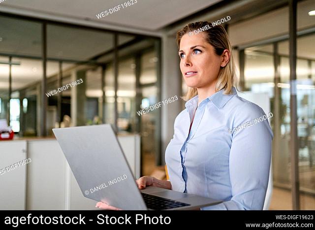 Thoughtful businesswoman holding laptop at office