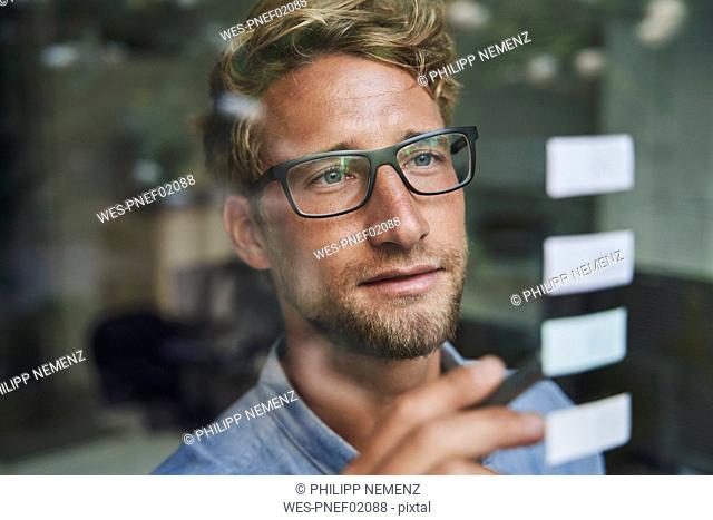 Casual young businessman with adhesive notes behind windowpane in office