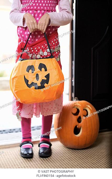 Detail of girl wearing Halloween costume holding Jack-O-Lantern candy basket
