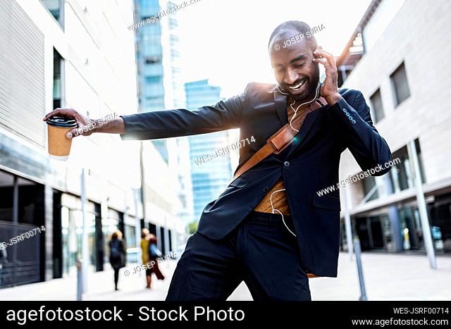 Portrait of happy young businessman dancing on the street while listening music with earphones