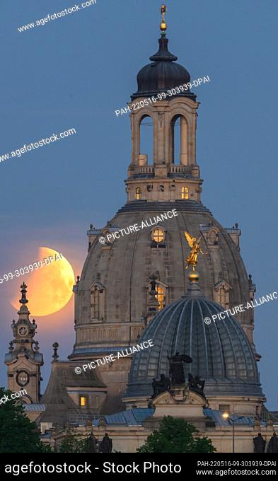 16 May 2022, Saxony, Dresden: The moon sets in the morning during a partial lunar eclipse behind the Frauenkirche and the dome of the Kunstakedmie with the...