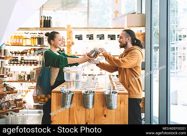 Smiling woman giving mason jar to man at counter in shop