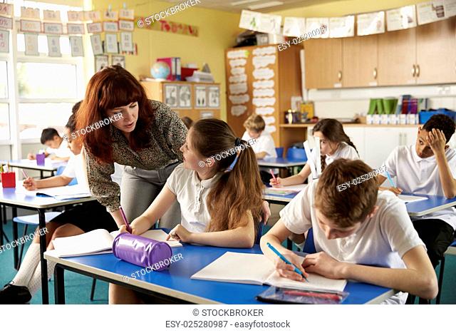 Primary school teacher helps a pupil at desk with classwork