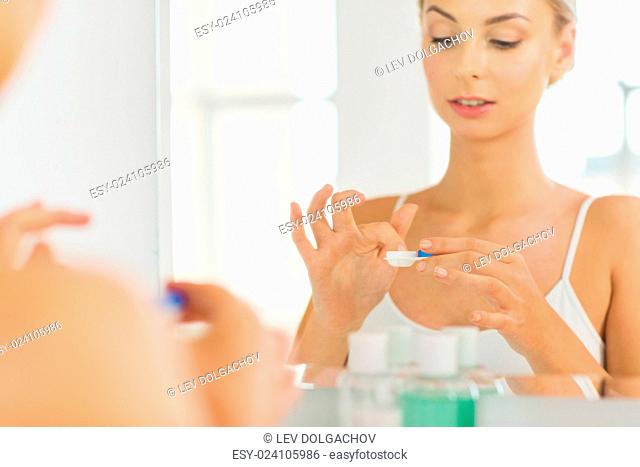 beauty, vision, eyesight, ophthalmology and people concept - close up of young woman applying contact lenses at mirror in home bathroom