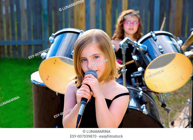 Blond kid girl singing in tha backyard with drums behind