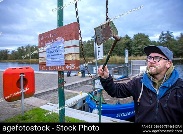 PRODUCTION - 26 October 2023, Mecklenburg-Western Pomerania, Stolpe: A man strikes an iron at the jetty of the small passenger ferry across the Peene and uses...