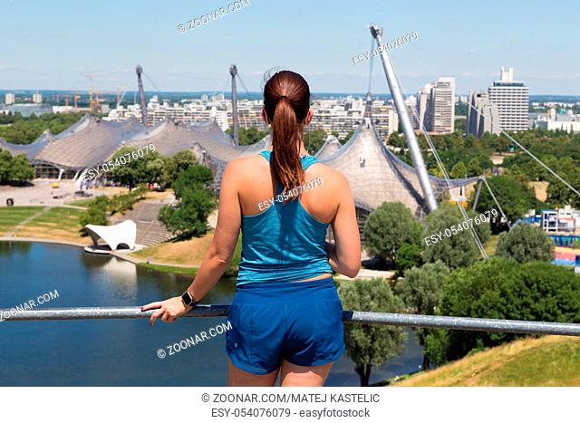 Female jogger relaxing after working-out listening to music enjoying the view over Munich olympic park