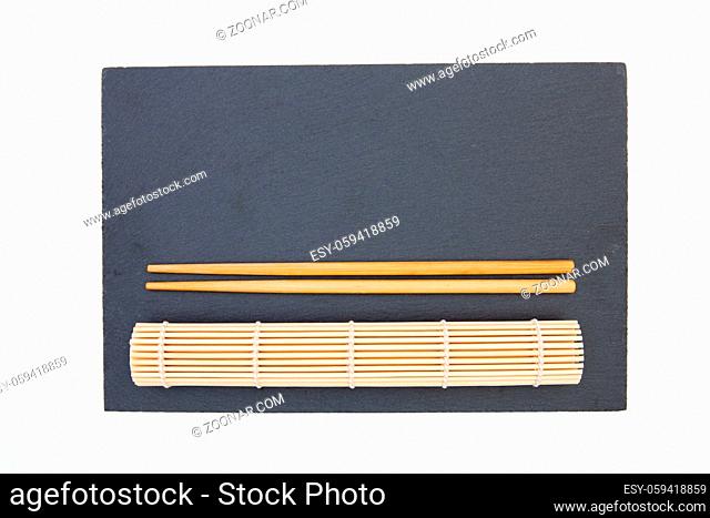 Rectangular slate plate with chopsticks, bamboo mat for sushi on the white table. Food Design