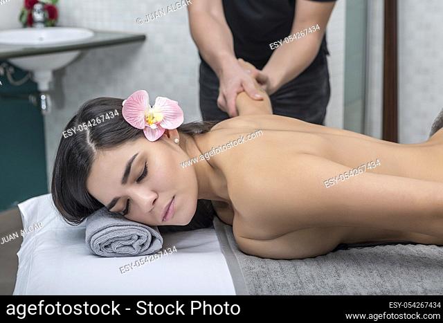 Crop man stretching and massaging sensual young woman lying topless on table in massage center