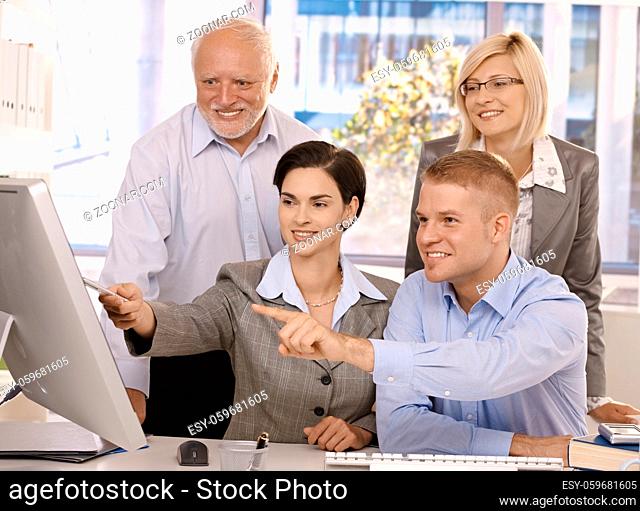 Smiling businessteam working together in office, looking at computer screen, pointing