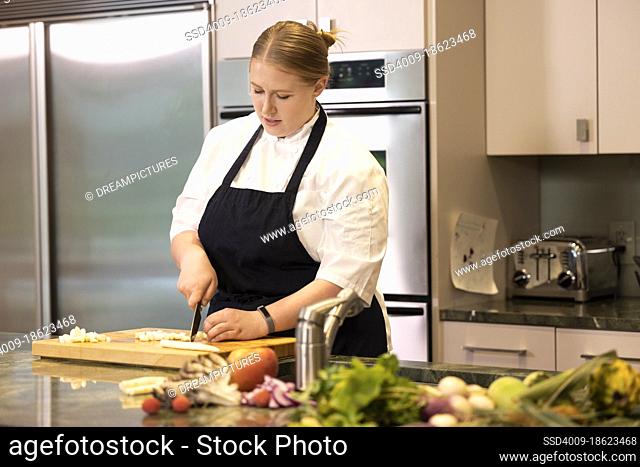 Professional Chef Megan Gill in kitchen looking down while cutting up vegetables