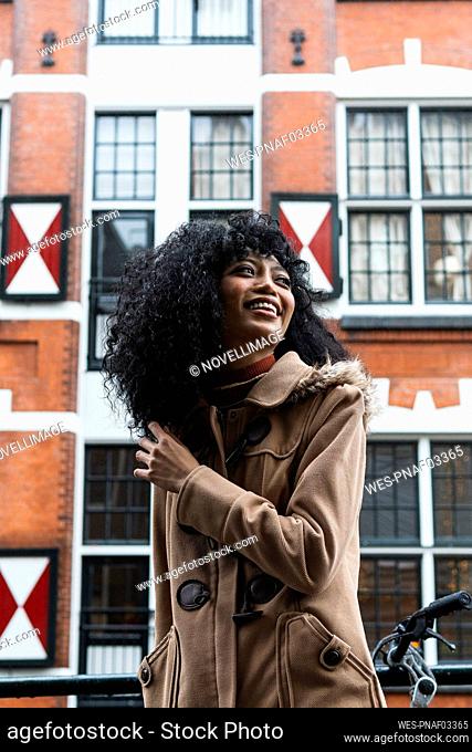 Happy woman with curly hair standing in front of building